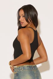 Woman wearing a black tank top and denim shorts on a plain background
