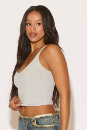 Woman wearing a gray crop top and blue jeans against a plain background