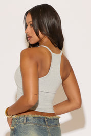Woman wearing a white tank top and blue jeans against a plain background