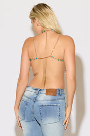 Model is wearing a multicolor beaded bralette top with fringe paired with denim jeans on a white background.