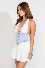 Model is wearing a lace halter bra cup with denim bustier top with a white skirt on a white background.