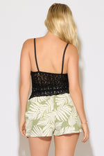 Model is wearing a black textured sheer lace v neck sleeveless cami top with green printed shorts on a white background.