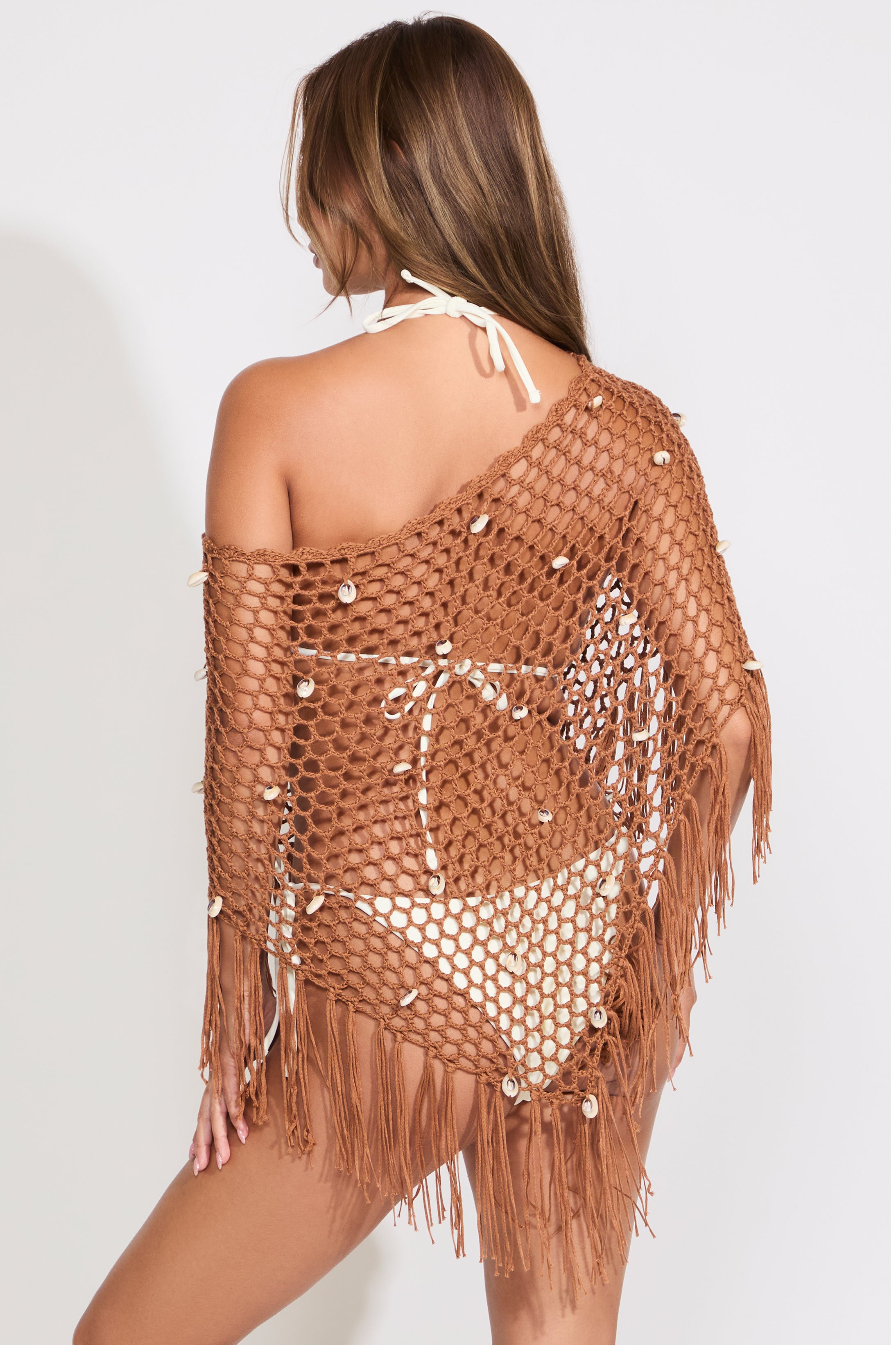 Model is wearing a brown open mesh boat neck poncho on top of a white bikini set on a white background.