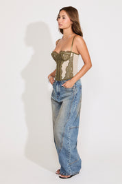 Model is wearing a green sheer lace sleeveless corset top with boning with jeans on a white background.