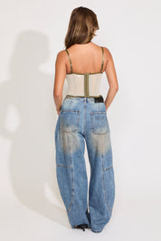Model is wearing a green sheer lace sleeveless corset top with boning with jeans on a white background.