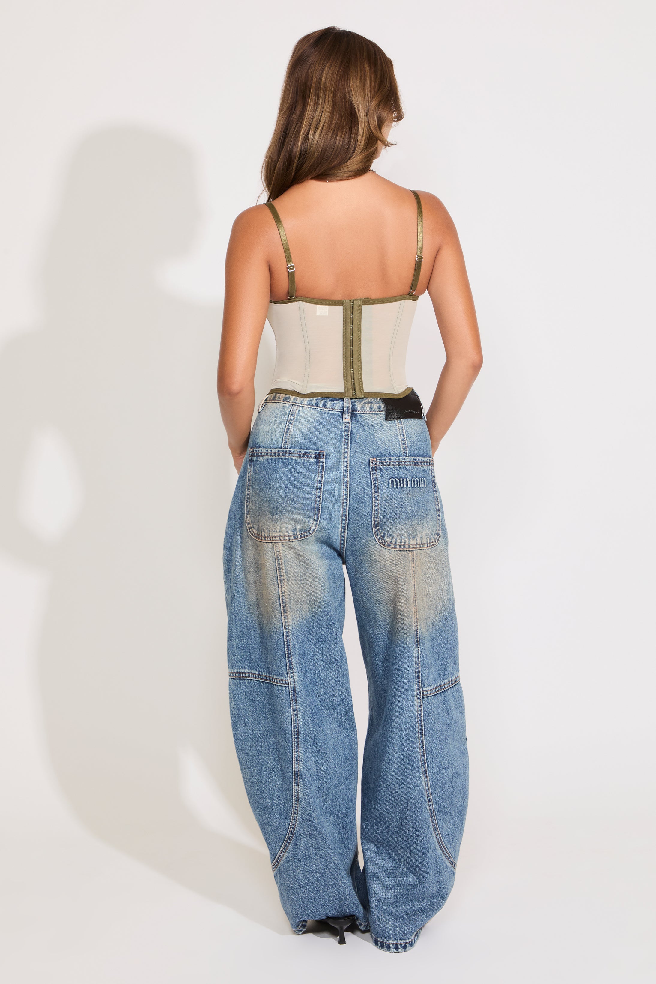 Model is wearing a green sheer lace sleeveless corset top with boning with jeans on a white background.