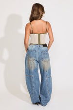 Model is wearing a green sheer lace sleeveless corset top with boning with jeans on a white background.