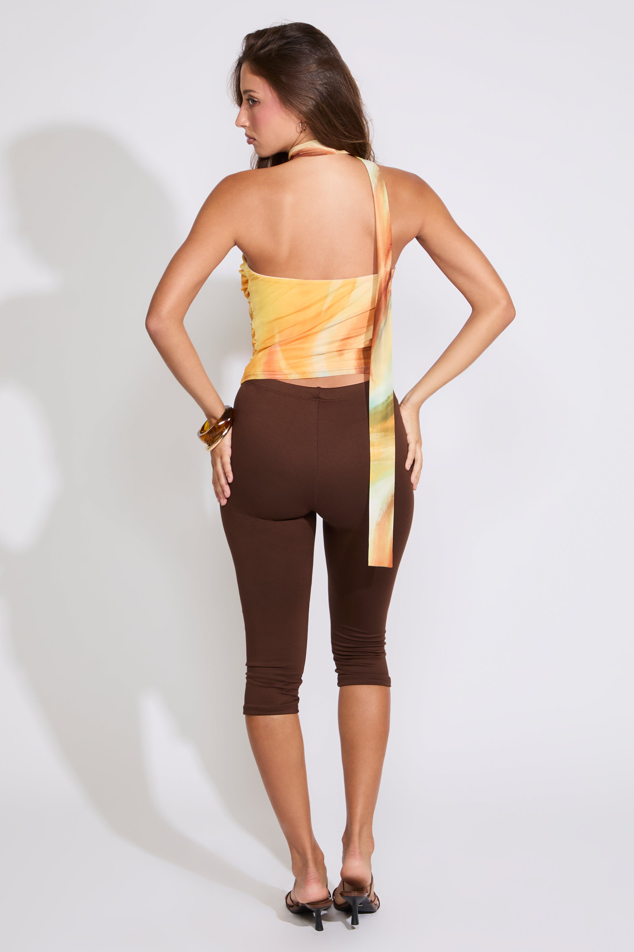 Model is wearing a yellow RUCHED MULTI COLOR STRAPLESS TOP WITH SCARF with brown capris and black heels on a white background. 