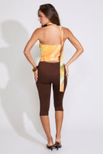 Model is wearing a yellow RUCHED MULTI COLOR STRAPLESS TOP WITH SCARF with brown capris and black heels on a white background. 