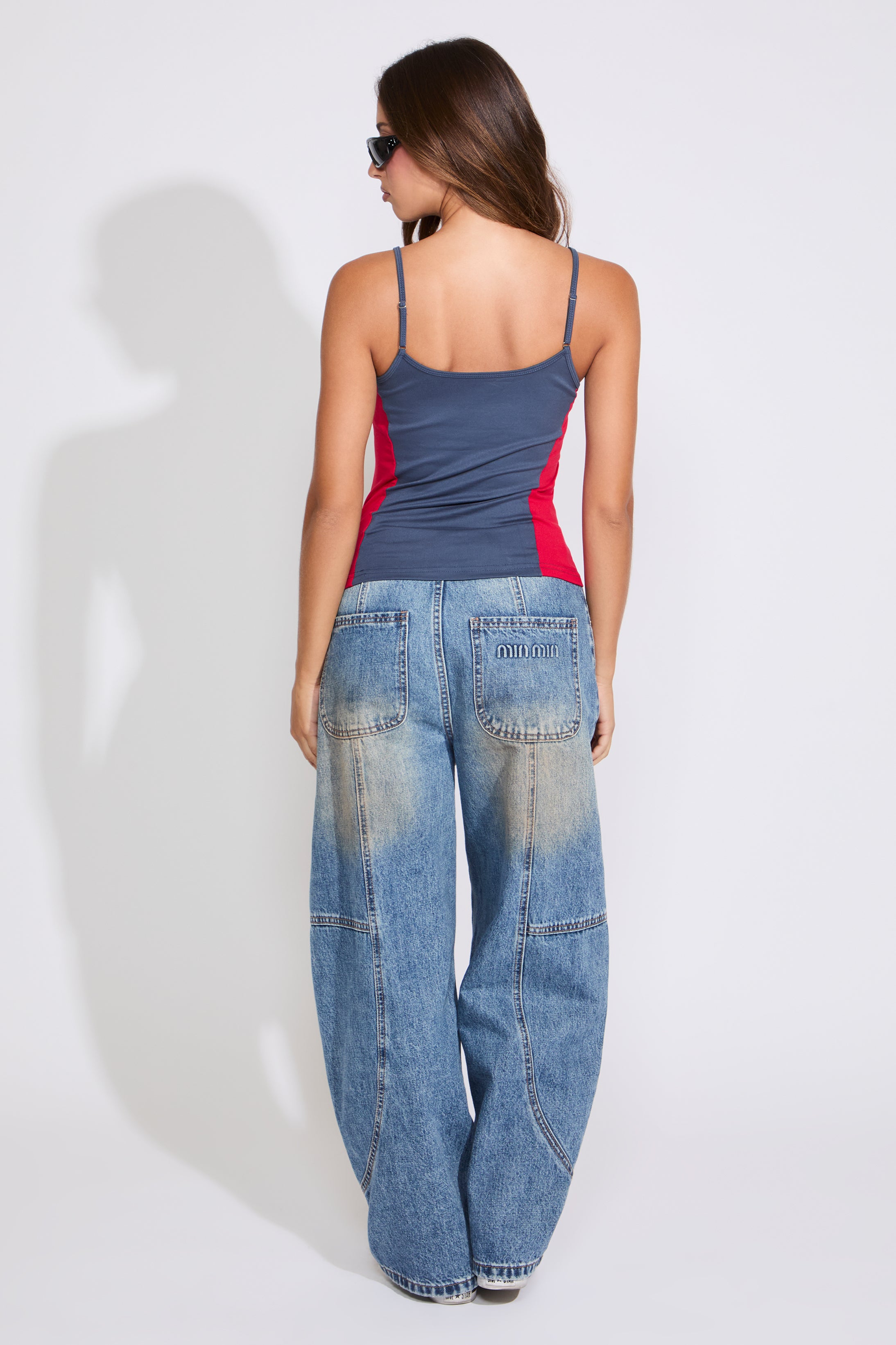 Model is wearing a navy COLOR BLOCK USA & FLAG LOGO SQUARE NECK CAMI TOP with medium denim jeans on a white background. 