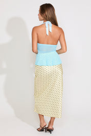 Woman wearing  a sheer blue top with a yellow and black polka dot skirt on a white background.