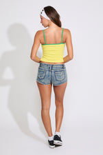 Model is wearing a yellow BRASIL NAME & FLAG CONTRAST STRAPS TANK TOP with denim shorts on a white background.