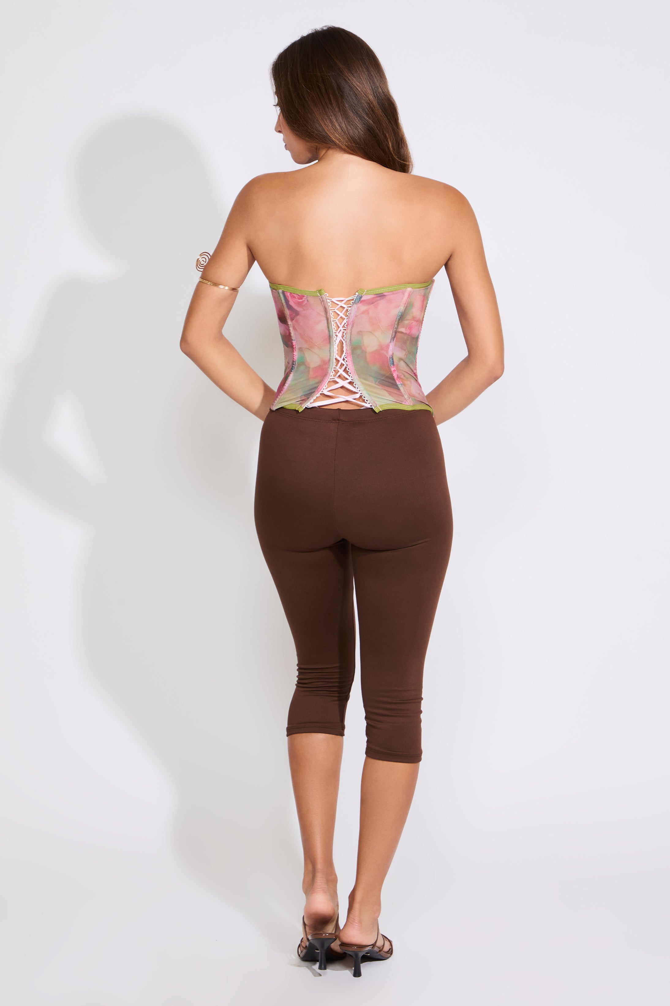 Model is wearing a RUCHED CUP FLORAL MESH CORSET TOP with brown capris on a white background.