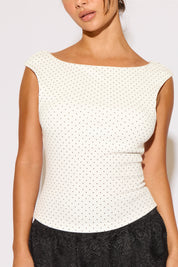 Woman wearing a white polka dot top with a plain background