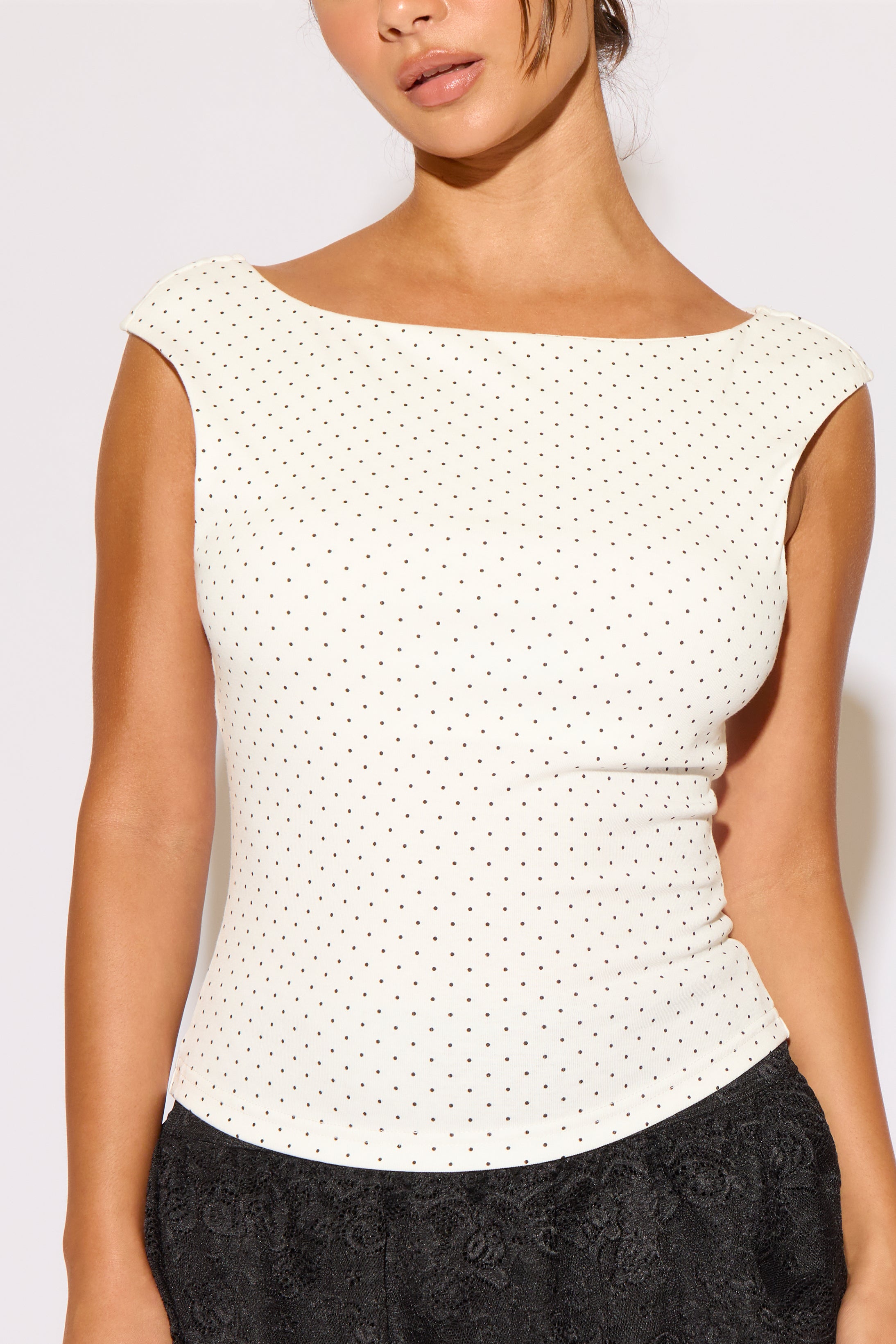Woman wearing a white polka dot top with a plain background