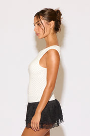 Woman wearing a white sleeveless top and black lace skirt against a plain background