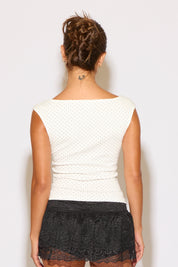 Person wearing a white sleeveless top with black lace trim on a plain background