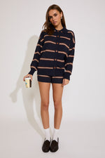 Woman wearing a navy striped sweater and shorts holding a coffee cup on a white background