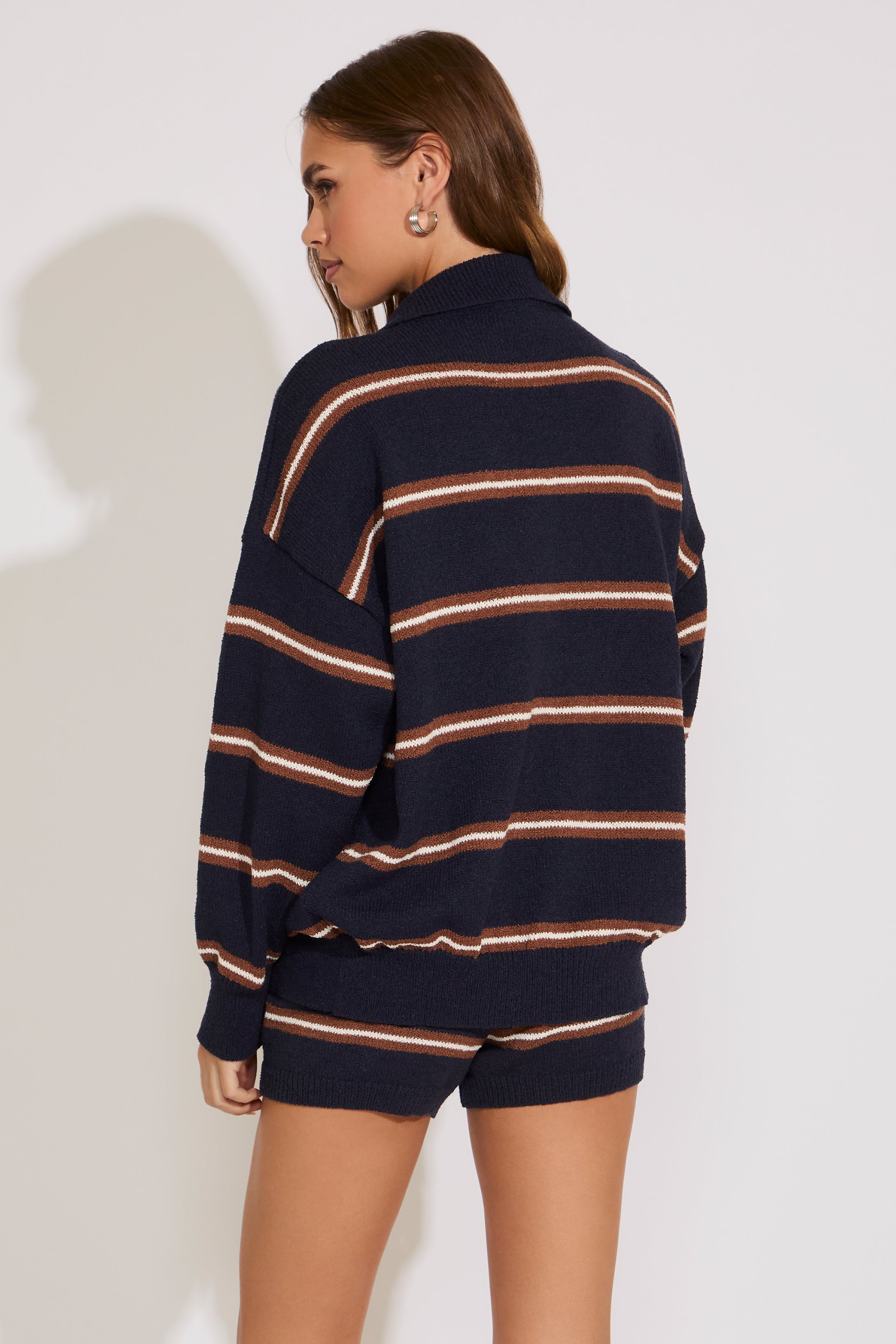 Person wearing a navy and beige striped sweater and shorts on a white background