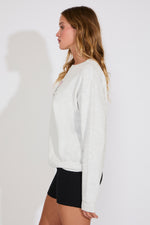Woman wearing a white sweatshirt and black shorts on a plain background