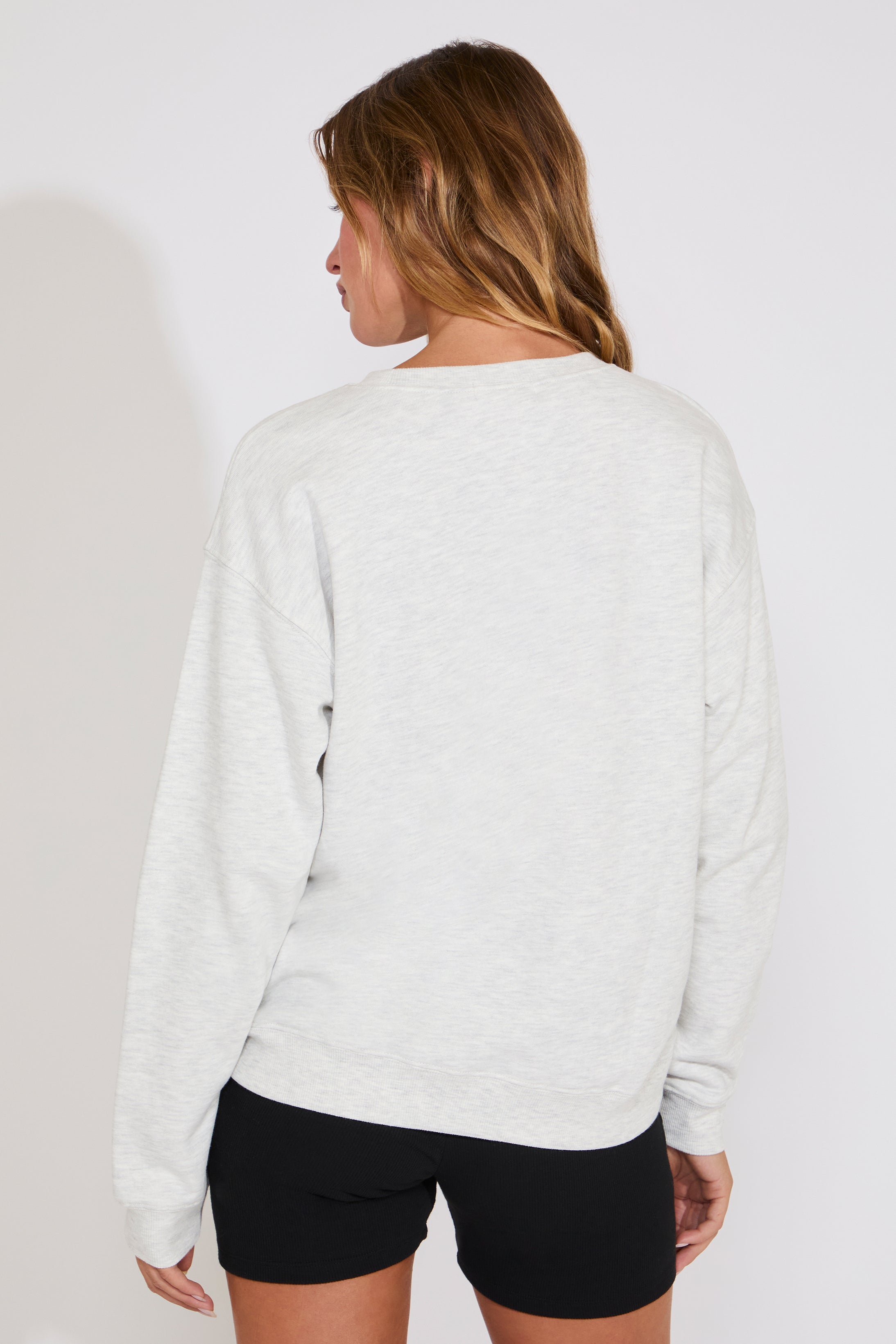 Person wearing a light gray sweatshirt and black shorts on a plain background