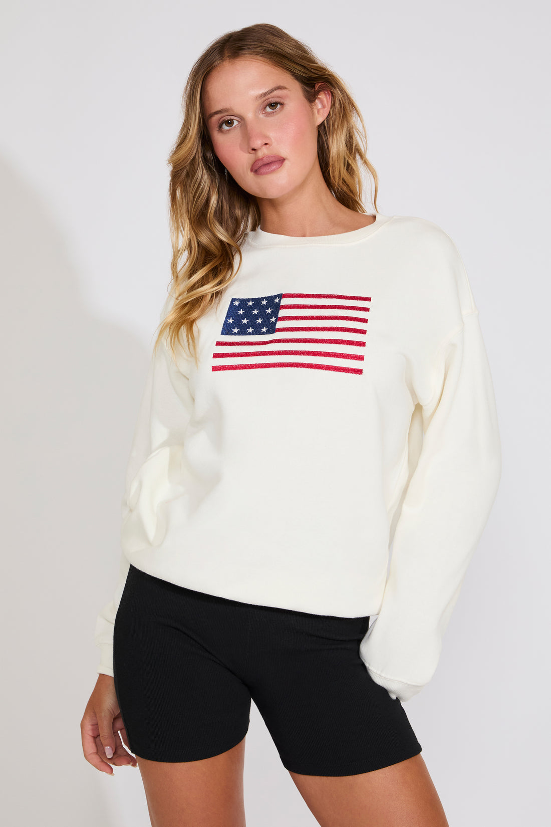 Woman wearing a white sweater with an American flag design on a plain background