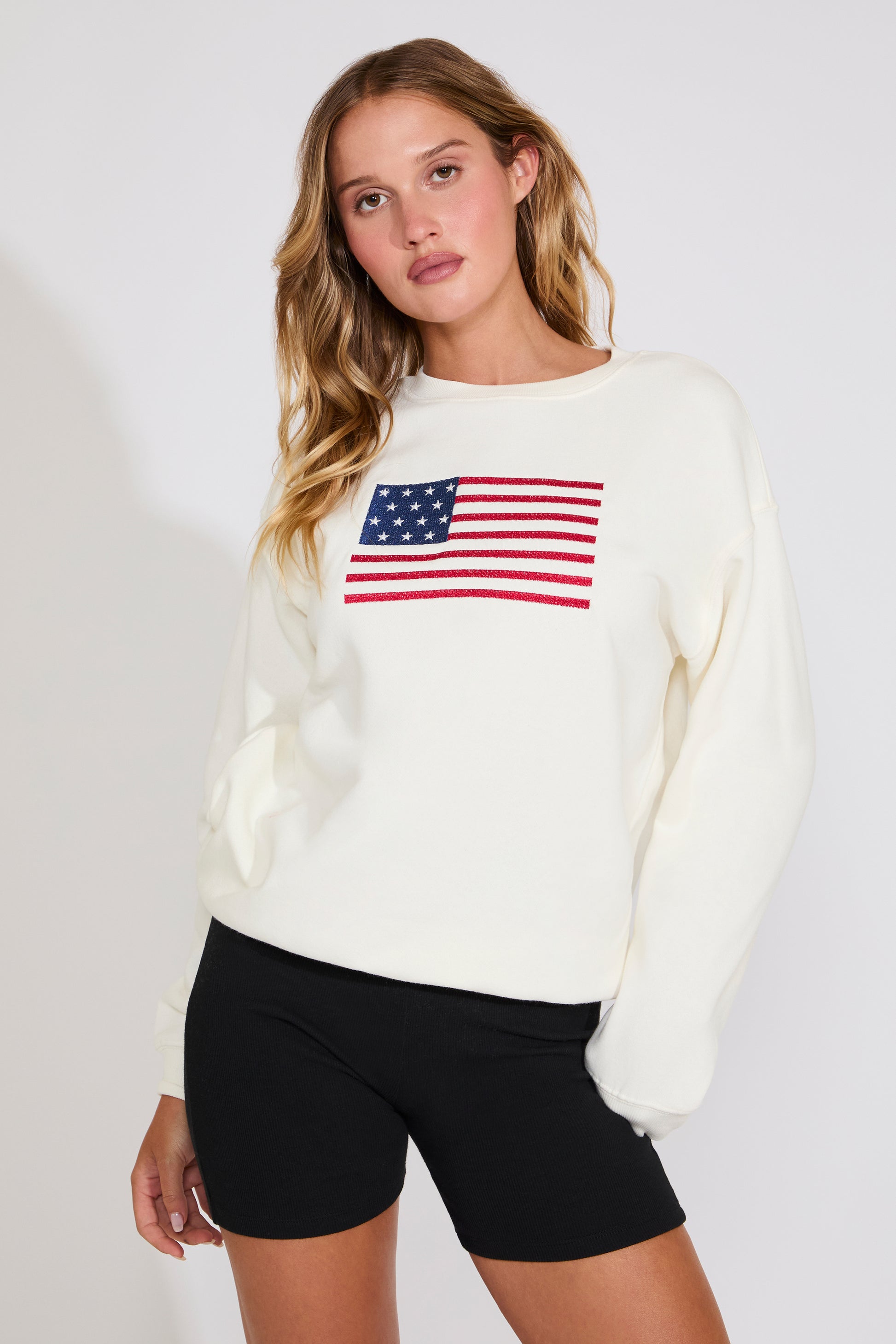 Woman wearing a white sweater with an American flag design on a plain background