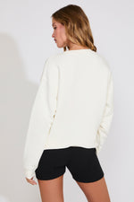 Woman wearing a white sweater and black shorts on a plain background