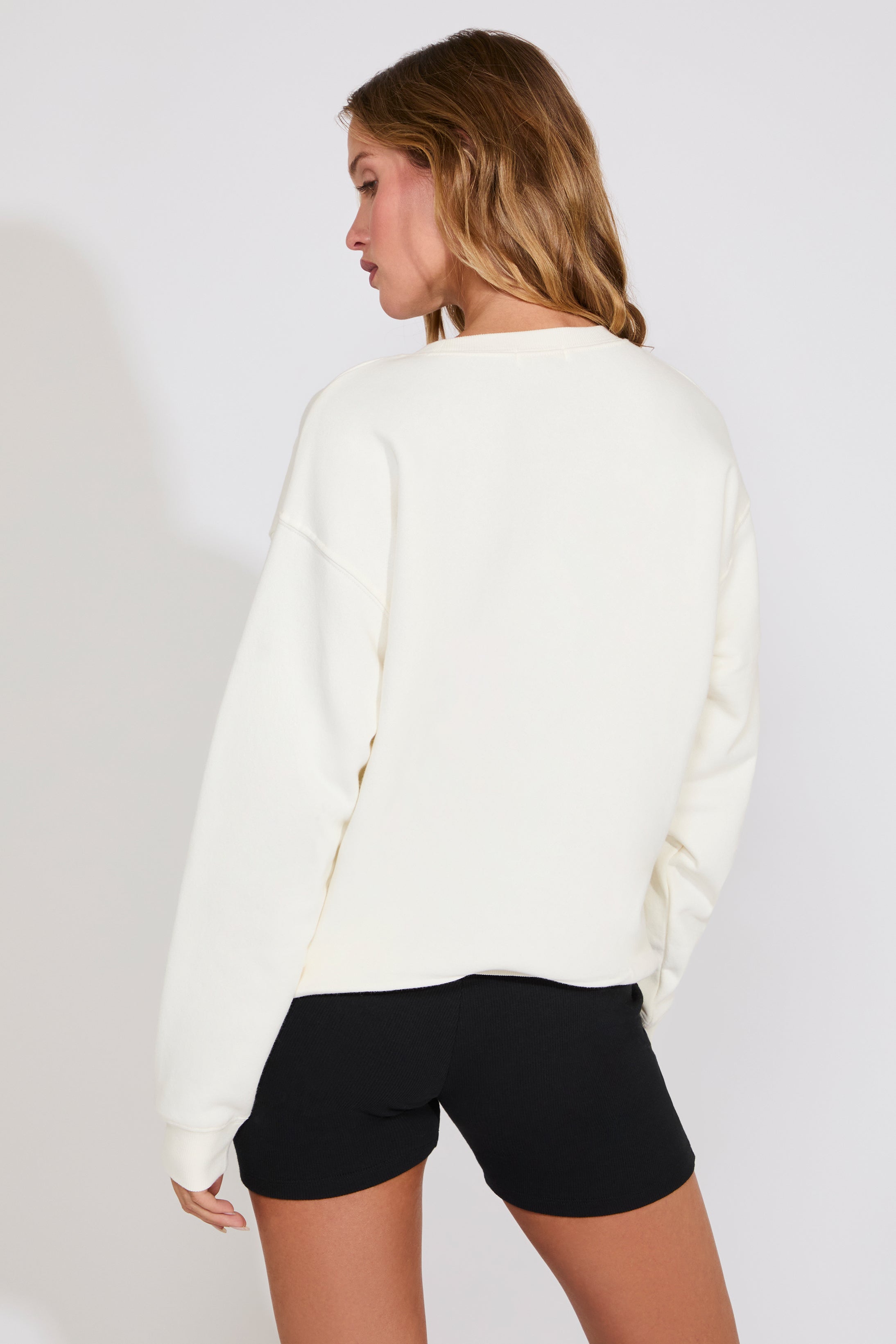 Woman wearing a white sweater and black shorts on a plain background