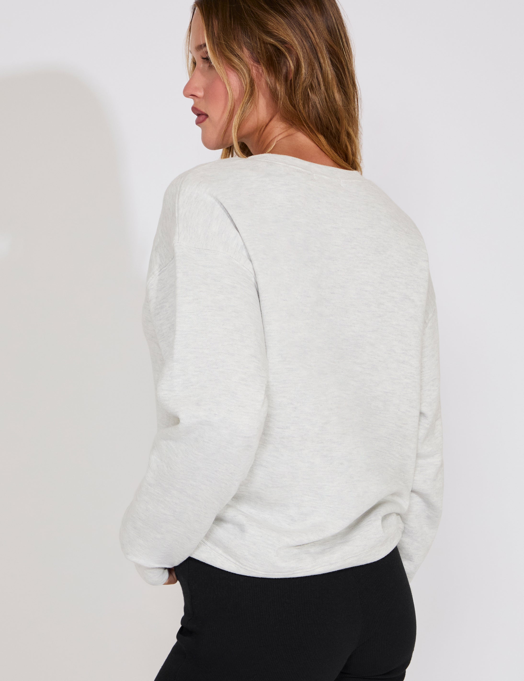 Woman wearing a light gray sweater and black pants against a white background