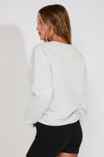 Woman wearing a light gray sweater and black pants against a white background