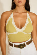 A female model wearing a yellow ribbed tank top with lace trim and a V-neckline, paired with white shorts.