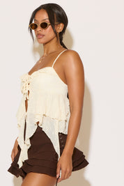 Woman wearing a white ruffled top and brown shorts against a plain background