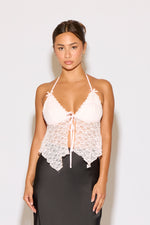 Woman wearing a white lace halter top and black pants on a light gray background