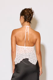 Woman wearing a white lace top and black pants against a plain background