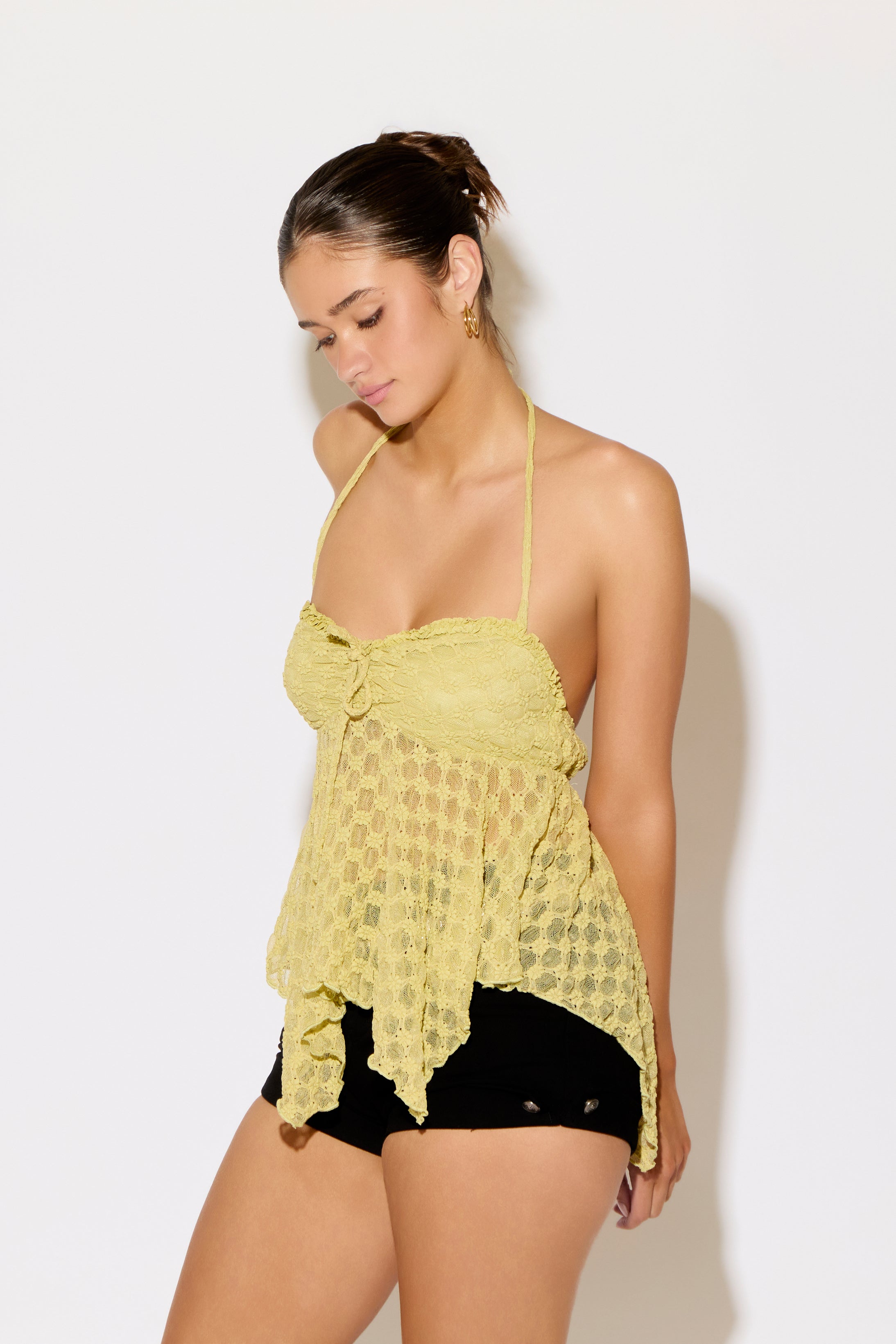 Woman wearing a yellow lace top and black shorts against a white background