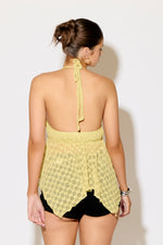 Woman wearing a yellow patterned top and black shorts against a white background