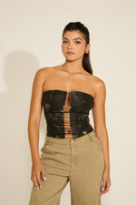 A woman wearing a strapless vegan leather top with an open middle cutout and distressed detailing, paired with beige trousers.