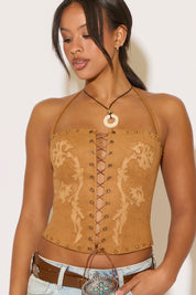 Woman wearing a tan embroidered halter top with decorative elements on a plain background