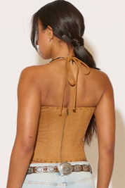 Woman wearing a tan halter top with decorative straps against a plain background