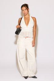 Woman wearing a white sleeveless top and wide-leg pants with a black handbag on a white background