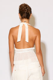 Woman wearing a white crochet top with open back against a light background