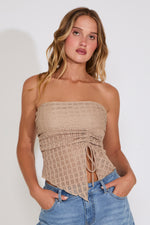 Woman wearing a beige strapless top and blue jeans against a white background