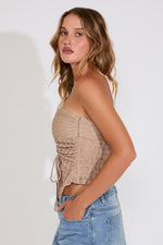 Woman wearing a beige strapless top and blue jeans against a white background