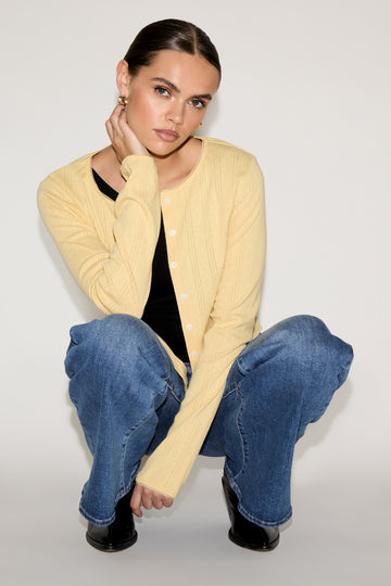 Woman wearing a yellow cardigan and blue jeans sitting on a white background