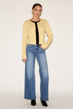 Woman wearing a yellow cardigan, black top, and blue jeans on a white background