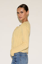 Woman wearing a yellow sweater and blue jeans against a plain background