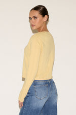 Woman wearing a yellow sweater and blue jeans against a white background