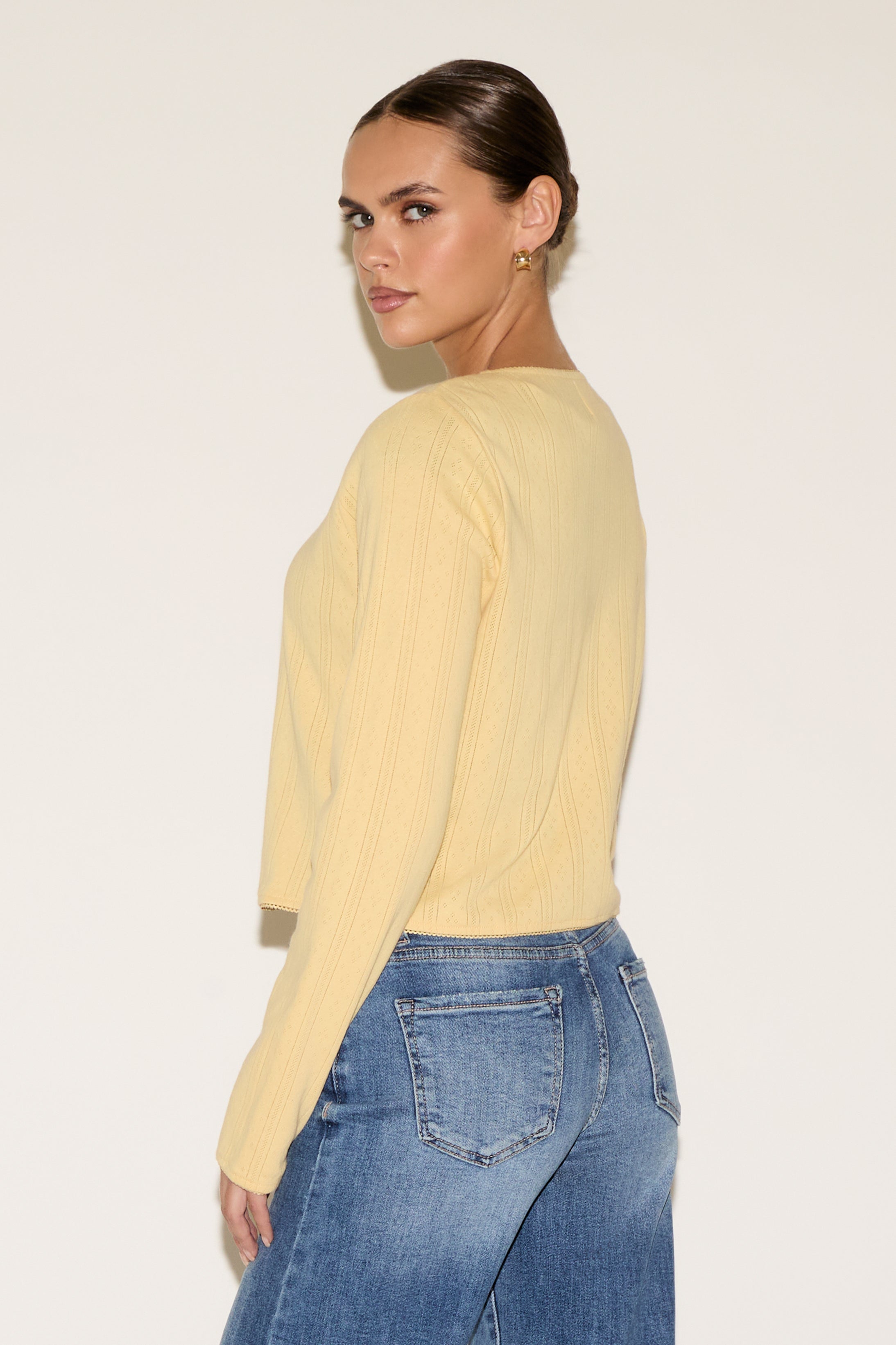 Woman wearing a yellow sweater and blue jeans against a white background