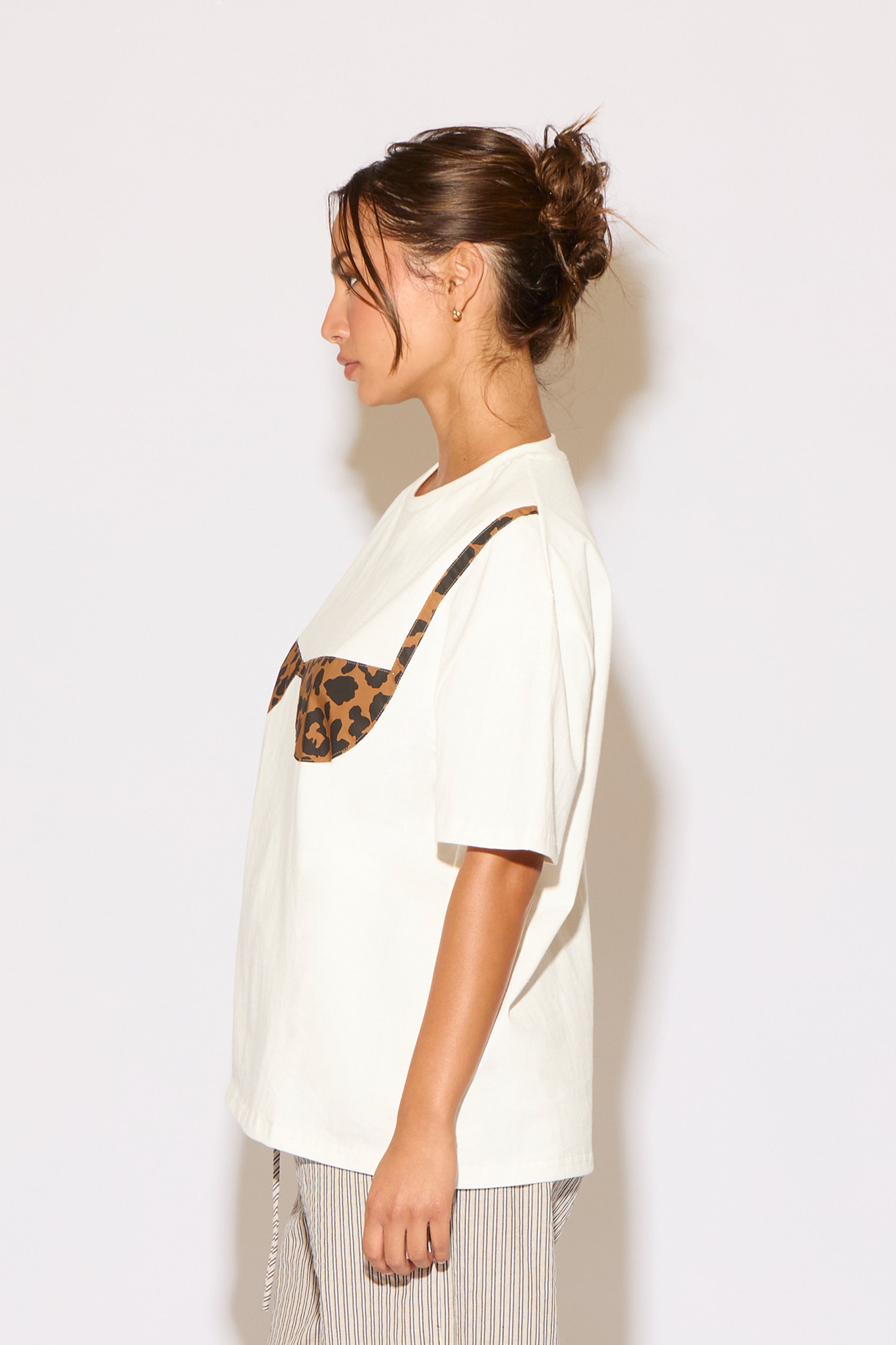 Woman wearing a white t-shirt with a leopard print design on a plain background